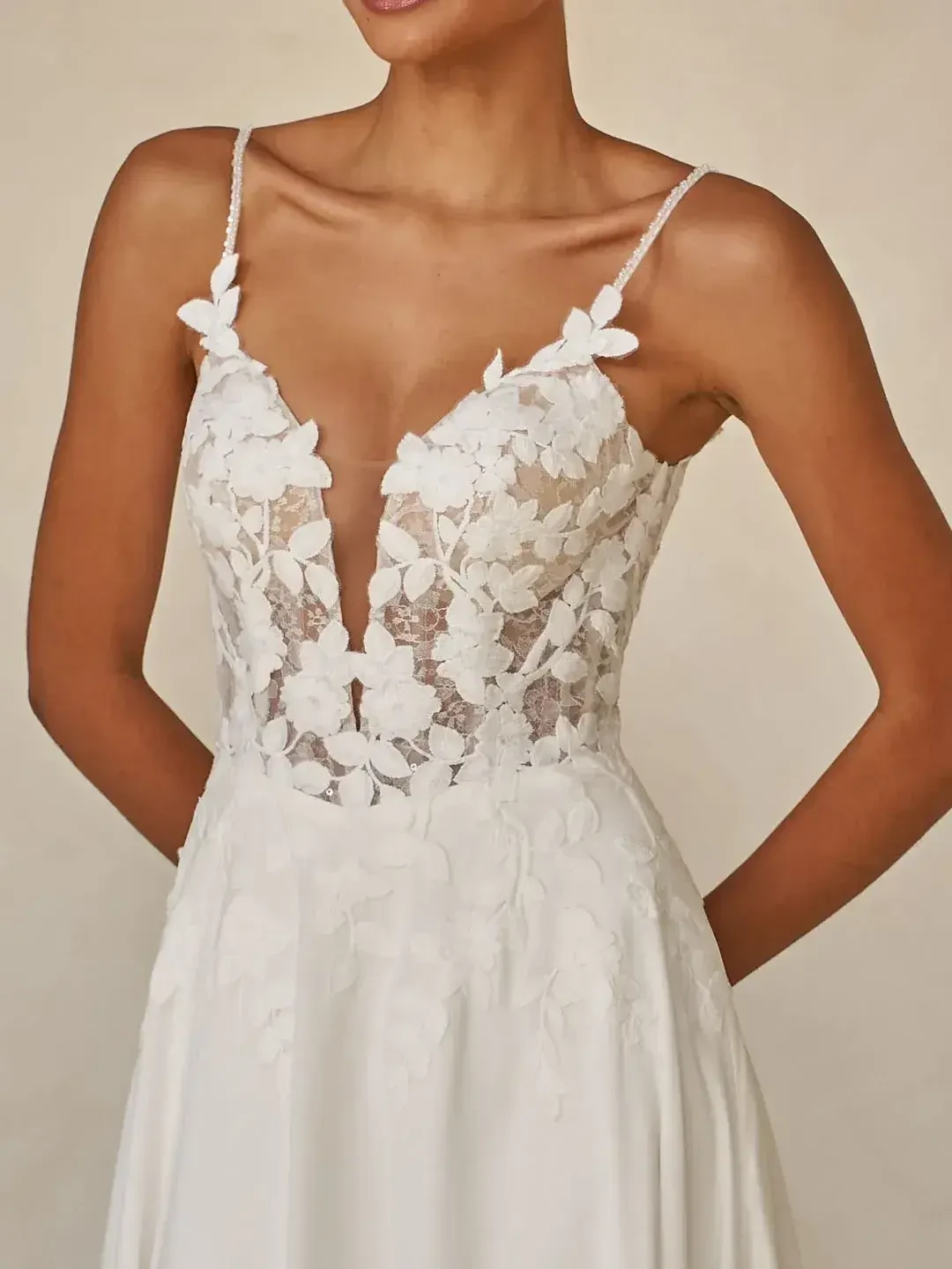 A woman in a bridal gown with a deep V-neck adorned with floral lace. The elegant dress exudes romance and sophistication against a neutral background.