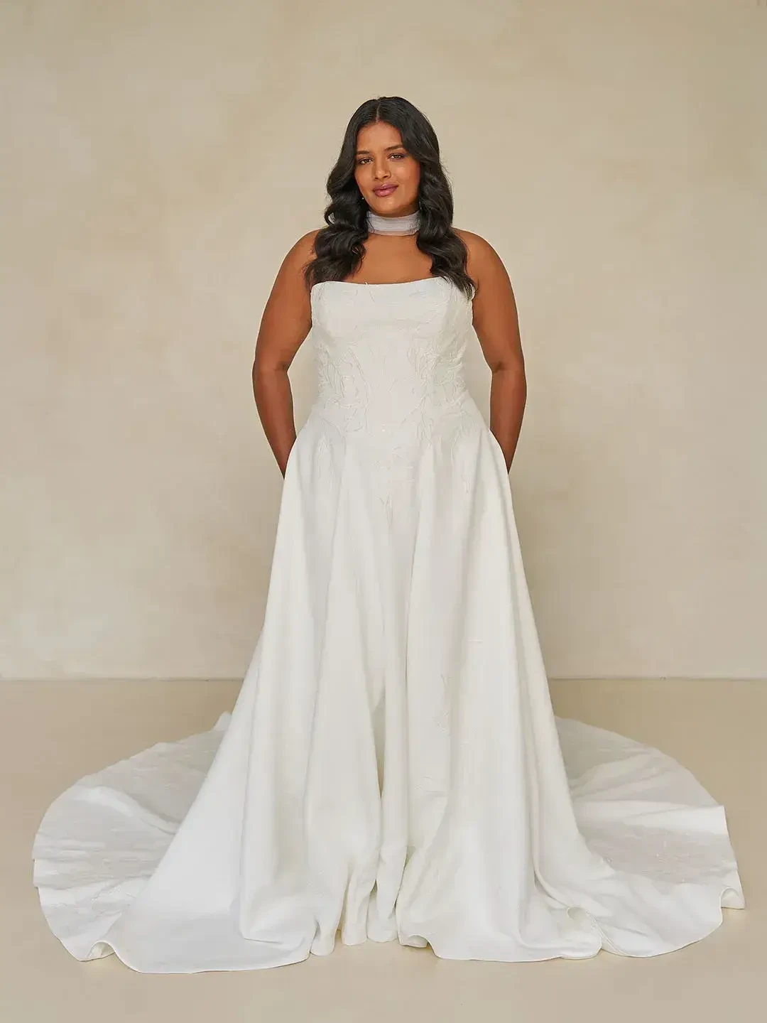 A person wearing a white strapless gown with a long train, standing against a neutral background.